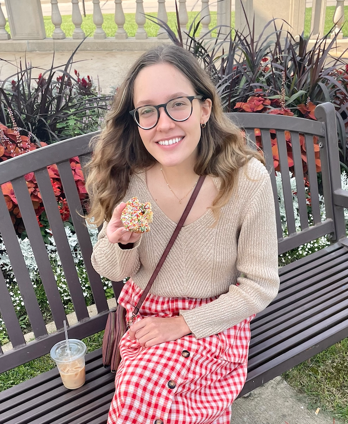 Photo of Rae sitting on a bench eating a donut.